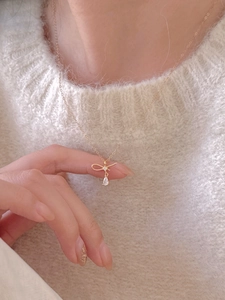 Détail d'un collier doré avec pendentif nœud et zircon goutte d'eau sur un pull moelleux