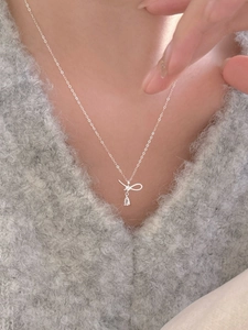 Gros plan du collier nœud en argent 925 avec zircon goutte sur pull gris doux