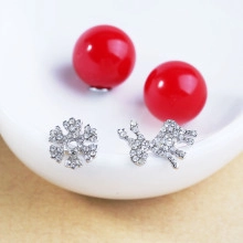 Detail view of asymmetric snowflake and deer earrings with festive red backings