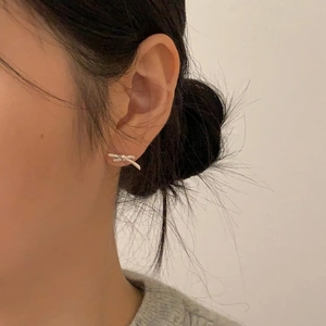 Close-up of minimalist silver bow stud earrings worn by a model in a soft-lit side view