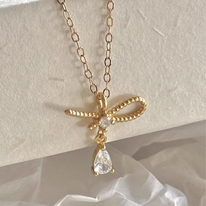 Collier nœud doré avec pendentifs en zircon sur un fond chaleureux et épuré