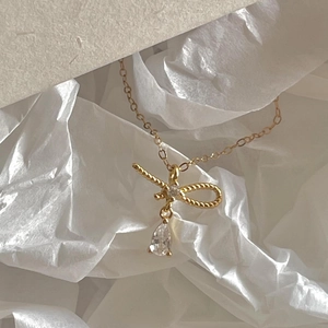 Gros plan sur un pendentif nœud doré avec zircon goutte sur fond élégant texturé