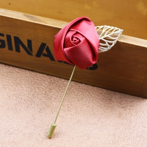 Handmade red satin rose brooch with silver leaf and long pin on a wooden box background