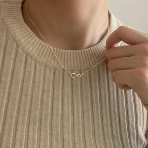 Close-up of silver infinity pendant necklace worn by a model on a beige knit sweater