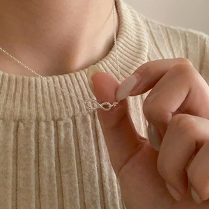 Close-up of minimalist silver infinity pendant necklace worn on a beige knit sweater