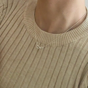 Close-up of minimalist S925 sterling silver infinity necklace worn on a beige sweater