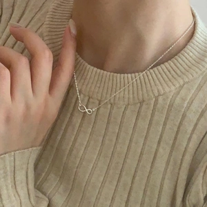 Detail of 925 sterling silver infinity pendant necklace on model with beige sweater