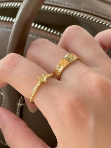Detail view of two gold rings with star motifs and hammered texture on female fingers