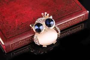 Detailed close-up of a gold owl brooch with blue crystal eyes and opal stone on a red book