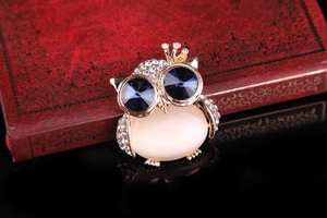 Detailed view of an owl brooch with blue crystal eyes and a white opal stone belly