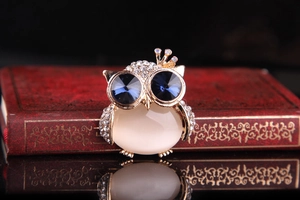 Macro shot of owl brooch with blue crystal eyes and opal belly on vintage red book