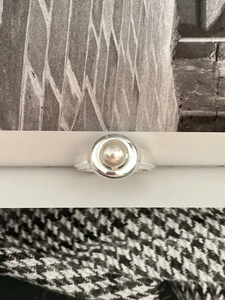 Close-up of minimalist 925 sterling silver ring with a white pearl in a wide circular setting
