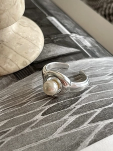 Detail of adjustable silver pearl ring with glossy wide band on stone surface