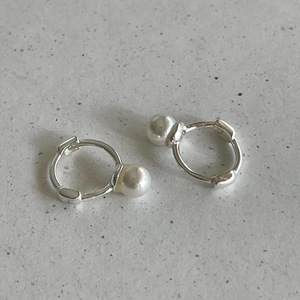 Detail of silver hoop earrings with white pearls on a minimalist stone background
