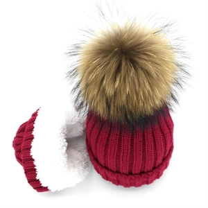 Detail of burgundy knit beanie with warm fleece lining and large faux fur pom pom