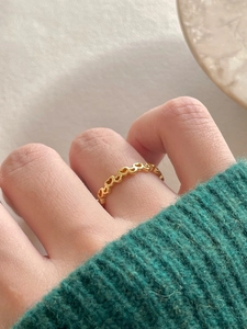 Close-up of golden heart-shaped hollow ring worn over a green sweater sleeve