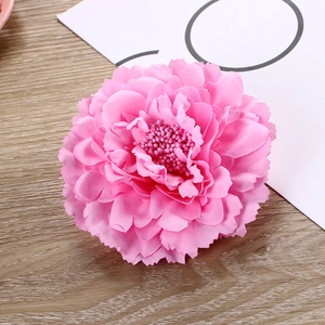 Close-up of a pink synthetic peony hair clip with layered petals on a wooden background