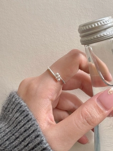 Detailed view of silver minimalist bead knot ring worn on hand with a soft knit sweater