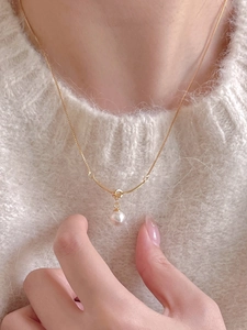 Detail of 925 silver knotted pearl necklace on model wearing a white sweater