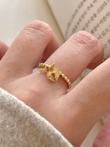 Detailed close-up of a gold heart-lock and key charm on a beaded silver open ring