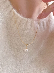 Close-up of gold 925 silver knot necklace with pearl pendant worn on neck