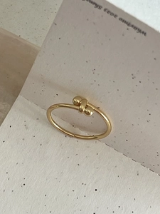 Macro detail of high-polished gold knot ring with double beads on a minimalist card