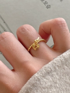 Close-up of golden beaded ring with heart lock and key charms on a model finger