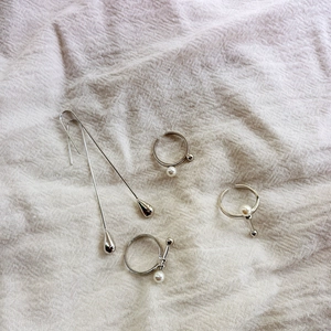 Boucles d'oreilles argentées et bagues en perles sur un fond en tissu beige texturé