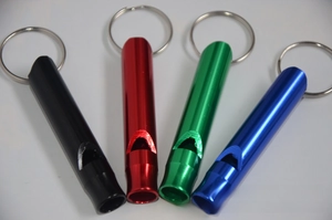 Detail view of four colorful aluminum survival whistles with keychains in a flat lay
