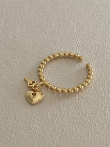 Detailed shot of golden bead ring featuring heart lock and key charms with open band