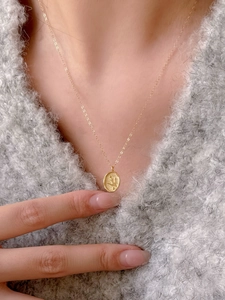 Close-up of golden oval coin pendant with embossed bird on a delicate chain necklace