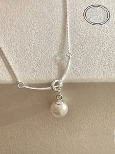Close-up of minimalist silver knot necklace with a round pearl on a beige gift box
