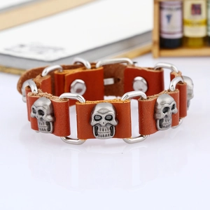 Close-up of brown leather punk bracelet with silver skull charms on reflective surface