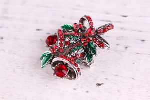 Close-up of Christmas bell brooch with red and green rhinestones on white wood texture