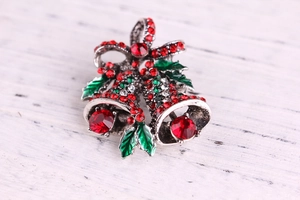 Macro shot of festive Christmas bell brooch with red and green rhinestones and enamel
