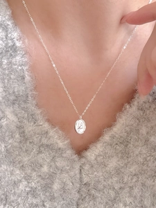 Macro view of sterling silver oval bird pendant on a grey knit sweater background