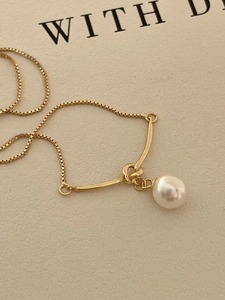 Detailed macro view of a gold knot pendant necklace with a round white pearl