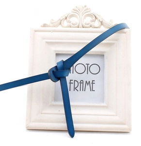 Detail view of a slim navy blue leather belt styled with a knot on a white frame