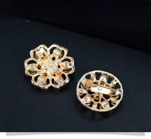 Vue détaillée de deux broches fleurs dorées avec fermoirs de sécurité sur fond de cuir noir