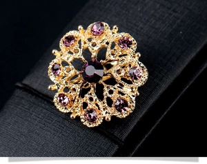 Détail d'une broche fleur dorée sertie de cristaux violets sur fond texturé