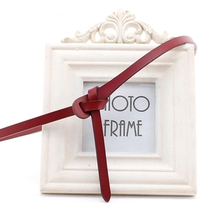 Close-up of a slim red leather belt tied in a knot on a vintage white frame