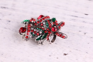 Macro detail of Christmas bell brooch with red and green rhinestones on white wood