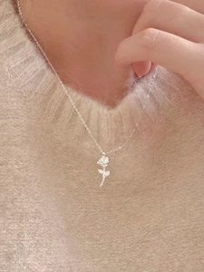 Detailed view of a silver rose flower pendant necklace worn on a beige knit sweater