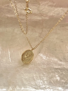 Detailed close-up of a gold-plated necklace featuring an oval swallow relief pendant