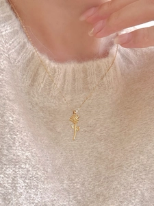Close-up of gold rose pendant necklace worn over a soft white mohair sweater