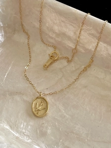 Macro shot of S925 hallmark on gold bird coin necklace with vintage embossed details