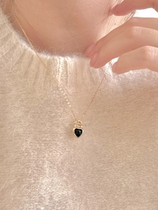 Close-up of a gold O-chain necklace featuring a black onyx heart padlock pendant on a model