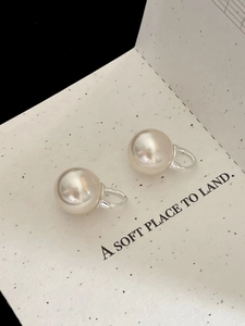 Detailed view of elegant cream pearl earrings with silver hooks on minimalist card