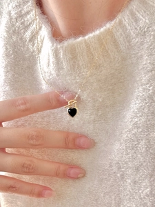 Detail of 925 silver gold necklace with black heart pendant on a soft knit sweater