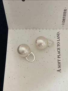 Detailed close-up of white pearl earrings with silver clasps on a textured display card